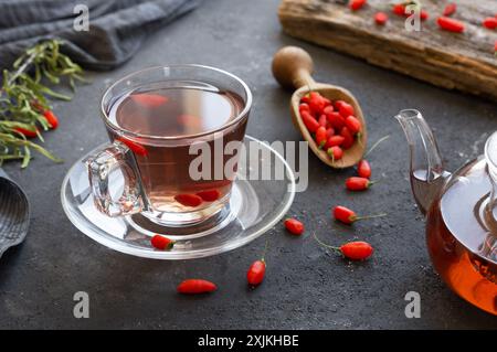 Tazza di tè alle erbe con bacche di goji fresche su tavola rustica Foto Stock