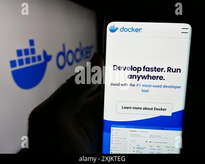 Persona che possiede lo smartphone con il sito Web della società di software per la produttività statunitense Docker Inc. Davanti al logo. Messa a fuoco al centro del display del telefono. Foto Stock