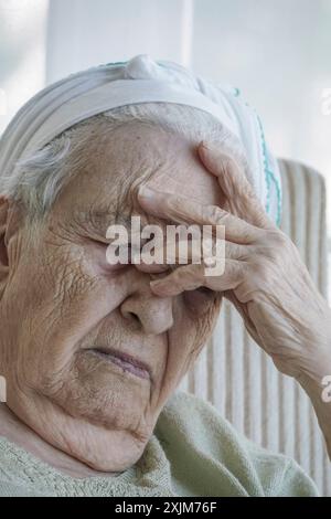 Una donna anziana che piange in una poltrona Foto Stock