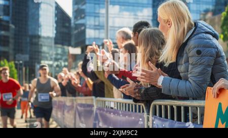 Il pubblico della maratona sostiene e incoraggia i propri cari che partecipano alla gara: Atletica maschile Marathon Runner tifo da parte di un membro della famiglia femminile nel pubblico durante la corsa Foto Stock