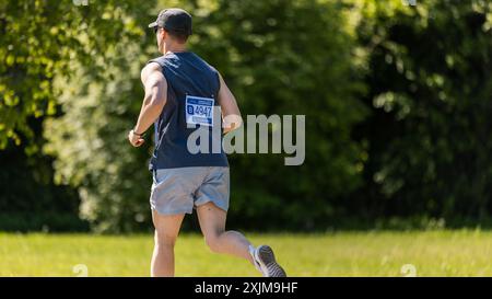 Ritratto di un giovane atletico maschile Jogger che corre in un parco su un sentiero della salute. Uomo sano e in forma godendo di attività fisica e rimanere in forma. Vista dal retro Foto Stock