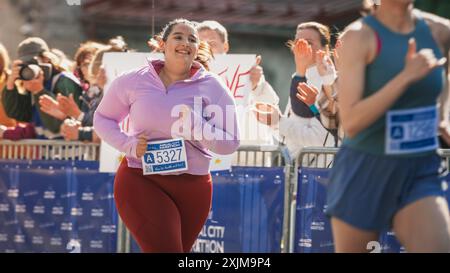 Ritratto di una Runner femminile sorridente Plus size che attraversa il traguardo e dimostra la sua forza di volontà. Simpatico pubblico della maratona cittadina che sostiene il pubblico Foto Stock