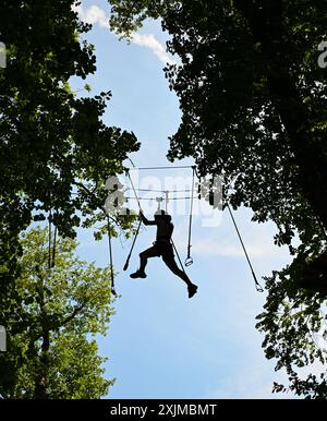 PRODUZIONE - 19 luglio 2024, Assia, Wiesbaden: Una giovane donna punta in alto nella foresta di arrampicata di Neroberg. Il parco di arrampicata per giovani ed esperti atleti ricreativi si trova sulla montagna locale di Wiesbaden, circondato da faggi e querce. Il punto più alto è un nido di avventura a un'altezza di 25 metri. Foto: Arne Dedert/dpa Foto Stock