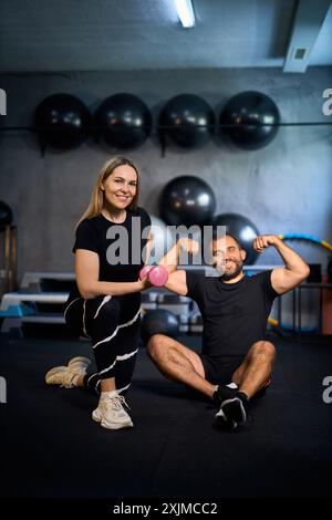 Felice coppia atletica che si flette i muscoli dopo un duro allenamento in palestra e guarda la macchina fotografica, sorridendo. Foto Stock
