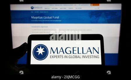 Stoccarda, Germania, 05-21-2022: Persona che detiene il cellulare con il logo della società Magellan Financial Group Limited sullo schermo davanti all'azienda Foto Stock