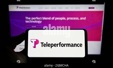 Stoccarda, Germania, 05-21-2022: Persona che detiene il cellulare con il logo della società francese di outsourcing Teleperformance se sullo schermo davanti alla pagina web. Foto Stock