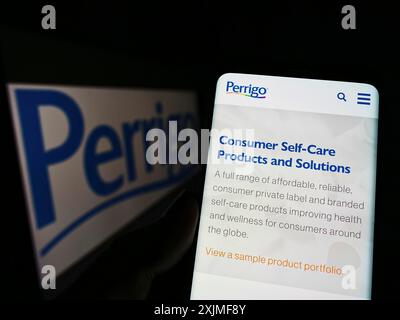 Stoccarda, Germania, 06-12-2022: Persona che detiene il cellulare con pagina web del produttore farmaceutico Perrigo Company plc sullo schermo con logo. Concentrati Foto Stock