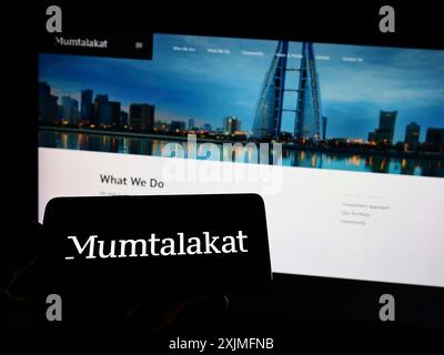 Stoccarda, Germania, 06-25-2022: Persona che detiene un cellulare con il logo della holding Mumtalakat del Bahrain sullo schermo di fronte alla pagina web aziendale. Foto Stock