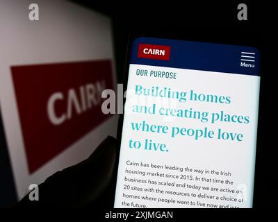 Stoccarda, Germania, 07-13-2022: Persona che detiene il cellulare con pagina web della società irlandese di costruzioni domestiche Cairn Homes plc sullo schermo davanti al logo. Foto Stock