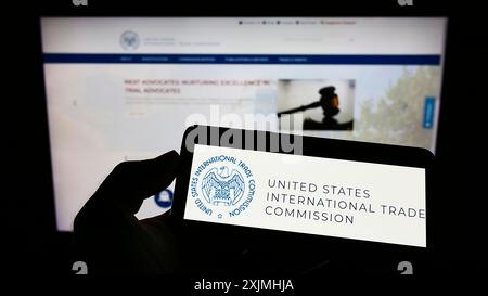 Stoccarda, Germania, 07-24-2022: Persona che detiene un cellulare con il logo della American International Trade Commission (USITC) sullo schermo davanti alla pagina web. Foto Stock