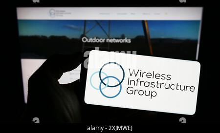 Stoccarda, Germania, 12-01-2022: Persona che detiene un cellulare con il logo della società Wireless Infrastructure Group (WIG) sullo schermo davanti all'azienda Foto Stock