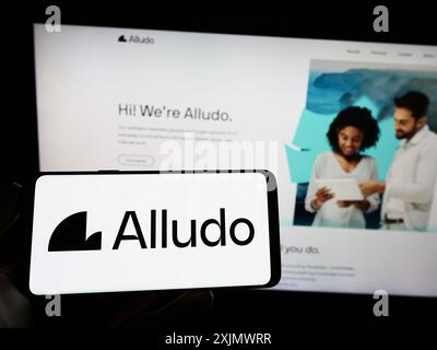 Stoccarda, Germania, 12-03-2022: Persona che detiene il cellulare con il logo della società Cascade Parent Limited (Alludo) sullo schermo di fronte alla pagina web aziendale. Foto Stock