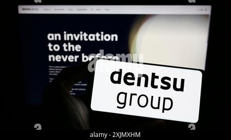 Stoccarda, Germania, 12-14-2022: Persona che detiene il cellulare con il logo della società pubblicitaria giapponese Dentsu Inc. Sullo schermo davanti all'azienda Foto Stock