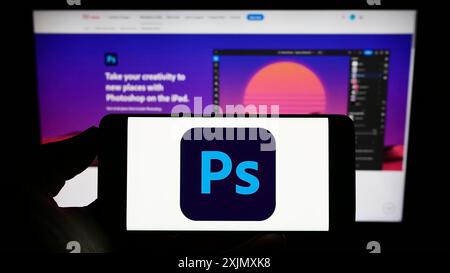 Stoccarda, Germania, 12-19-2022: Persona che tiene il cellulare con il logo del software di grafica Adobe Photoshop sullo schermo di fronte all'azienda Foto Stock