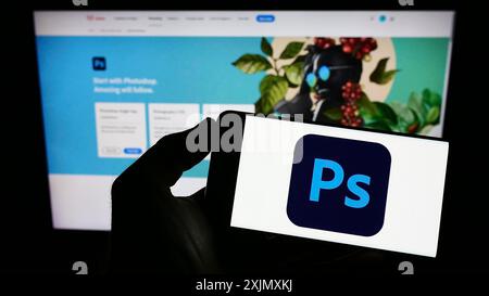 Stoccarda, Germania, 12-19-2022: Persona con smartphone con logo del software di grafica Adobe Photoshop sullo schermo davanti al sito Web. Concentrati Foto Stock