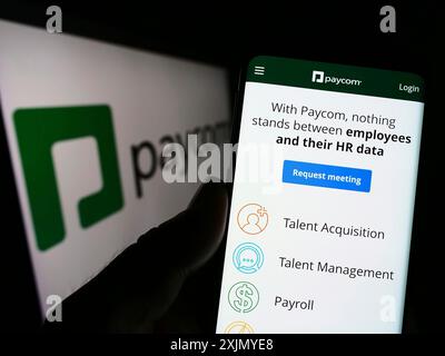 Stoccarda, Germania, 12-31-2022: Persona che detiene lo smartphone con pagina web della società di tecnologia Paycom software Inc. Sullo schermo con logo. Concentrati Foto Stock