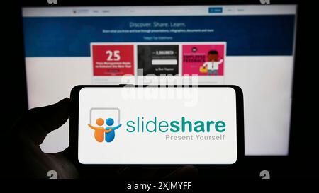 Stoccarda, Germania, 12-31-2022: Persona che detiene un cellulare con il logo della società di hosting di contenuti SlideShare sullo schermo di fronte alla pagina Web aziendale. Foto Stock