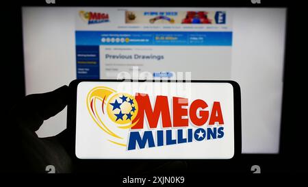 Stoccarda, Germania, 01-13-2023: Persona che tiene il cellulare con il logo della lotteria USA Mega Millions sullo schermo davanti alla pagina web. Mettere a fuoco il display del telefono Foto Stock