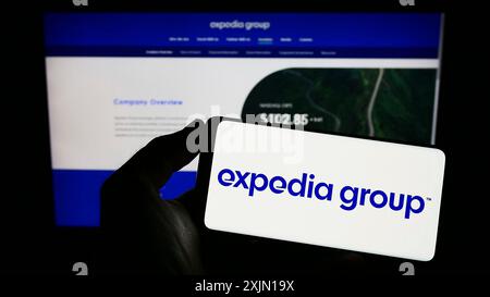 Stoccarda, Germania, 01-12-2023: Persona che possiede un telefono cellulare con il logo della società di viaggi online americana Expedia Group Inc. Sullo schermo davanti al web Foto Stock