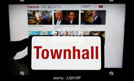 Stoccarda, Germania, 01-13-2023: Persona che tiene un cellulare con il logo del sito web di notizie conservatrici degli Stati Uniti Townhall sullo schermo di fronte alla pagina web dell'azienda. Foto Stock