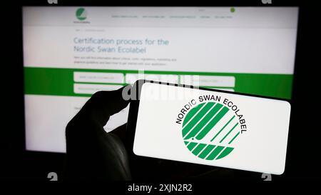 Stoccarda, Germania, 03-11-2023: Persona che detiene un cellulare con logo di certificazione ambientale Nordic Ecolabel sullo schermo davanti alla pagina web. Foto Stock