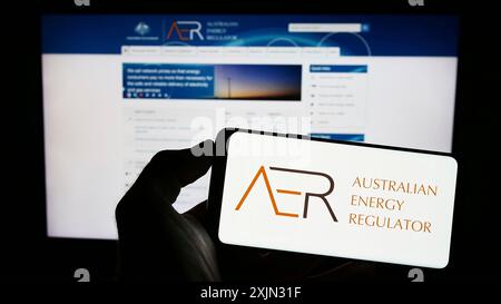 Stoccarda, Germania, 03-12-2023: Persona che detiene un cellulare con il logo dell'autorità dell'Australian Energy Regulator (AER) sullo schermo davanti alla pagina web. Foto Stock