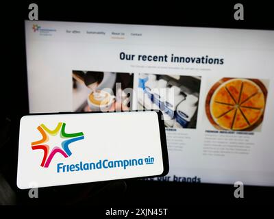 Stoccarda, Germania, 03-25-2023: Persona che detiene il cellulare con il logo della società Koninklijke FrieslandCampina N.V. sullo schermo davanti all’azienda Foto Stock