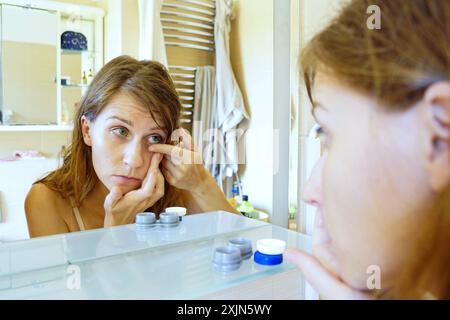 Foto di una giovane donna che indossa lenti a contatto colorate nel bagno di fronte a uno specchio. Routine quotidiana di una ragazza con miopia. Foto Stock