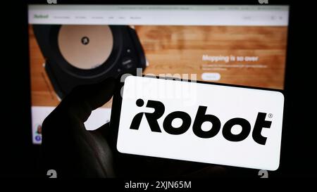 Stoccarda, Germania, 03-31-2023: Persona che tiene il cellulare con il logo della società tecnologica statunitense iRobot Corporation sullo schermo davanti all'azienda Foto Stock