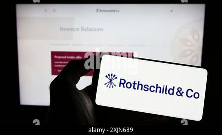 Stoccarda, Germania, 03-31-2023: Persona che tiene il cellulare con il logo della società di servizi finanziari Rothschild Co sullo schermo davanti all'azienda Foto Stock