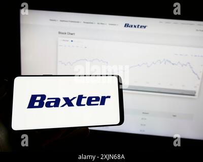 Stoccarda, Germania, 03-31-2023: Persona che tiene il cellulare con il logo della società sanitaria americana Baxter International Inc. Sullo schermo di fronte Foto Stock