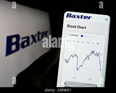 Stoccarda, Germania, 03-31-2023: Persona che tiene il cellulare con pagina web della società sanitaria statunitense Baxter International Inc. Su schermo con logo. Concentrati Foto Stock