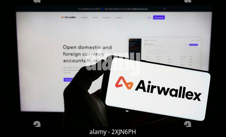 Stoccarda, Germania, 03-26-2023: Persona che detiene un cellulare con il logo della società di tecnologia finanziaria Airwallex sullo schermo di fronte alla pagina web aziendale. Foto Stock