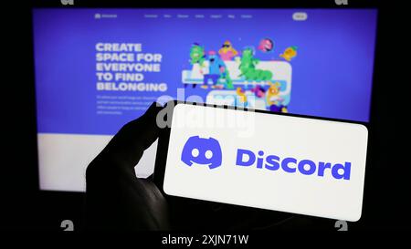 Stuttgart, Germania, 03-25-2023: Persona con smartphone con logo della società di social network statunitense Discord Inc. Sullo schermo davanti al sito Web. Concentrati su Foto Stock