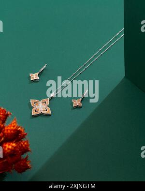 Elegante set di gioielli a forma di farfalla con dettagli arancioni e argento su sfondo verde. Foto Stock