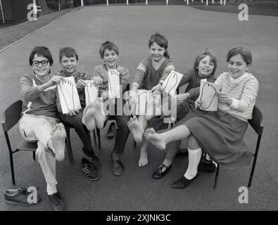 anni '1980, disegni dei piedi, un gruppo di bambini delle scuole seduti insieme in un parco giochi, a piedi nudi nell'aria, mostrando i disegni o tracciando che hanno fatto dei loro piedi. Inghilterra, Regno Unito. Foto Stock