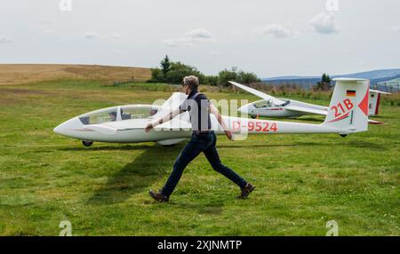 PRODUZIONE - 18 luglio 2024, Assia, Gersfeld (Röhn): Dierk Althoff, allievo di aliante, aiuta con il lancio di un velivolo da addestramento. La scuola di volo Wasserkuppe è la più antica scuola di volo in aliante del mondo: Ha 100 anni. Foto: Andreas Arnold/dpa Foto Stock