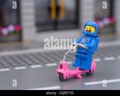 Tambov, Federazione Russa - 12 luglio 2024 Lego Benny astronauta minifigure in sella a uno scooter lungo una strada cittadina Foto Stock