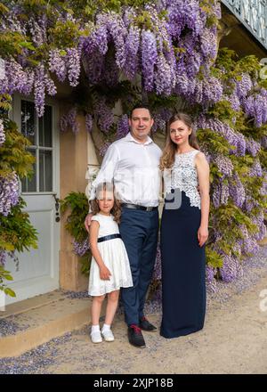 Ritratto di famiglia. Mamma, papa' e figlia. Mamma e ragazza sono vestiti con abiti bellissimi, papà indossa una camicia bianca. Sfondo floreale. Caldo, chiuso fa Foto Stock