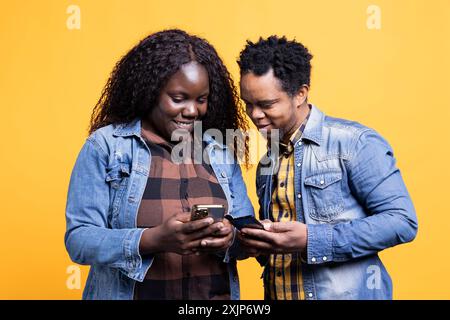 afroamericani che inviano messaggi sui loro telefoni cellulari, trascorrendo del tempo libero insieme in studio. Giovani compagni di anime sposati che si mostrano divertenti video in macchina. Foto Stock