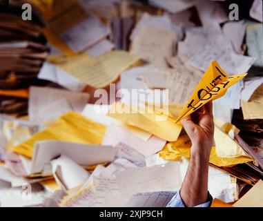 Un'immagine umoristica di una mano che regge un aereo di carta giallo con la scritta "i Quit", circondata da una pila di documenti. L'immagine sugg Foto Stock