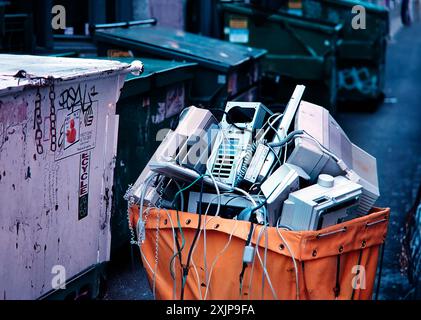Un contenitore di riciclaggio giallo è pieno di componenti del computer scartati, tra cui un monitor, una torre, una tastiera e altri componenti vari. Il Foto Stock