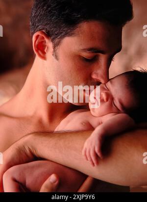 Un padre culla dolcemente il suo neonato tra le braccia, il suo viso si rivolge verso il bambino mentre bacia la fronte. Il bambino sta dormendo in quello del padre Foto Stock