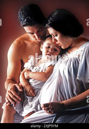 Una donna incinta siede con suo marito e sua figlia. La donna è seduta con la mano sinistra appoggiata sullo stomaco e la mano destra sul da Foto Stock