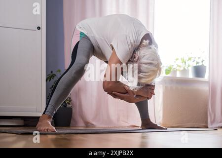 Donna anziana che fa pilates sul tappeto a casa Foto Stock