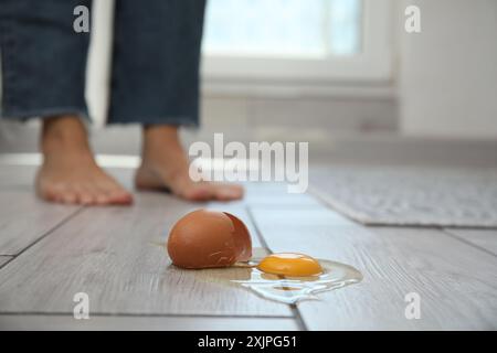 Donna vicina a un uovo crudo rotto su un pavimento in legno grigio in interni, messa a fuoco selettiva. Spazio per il testo Foto Stock