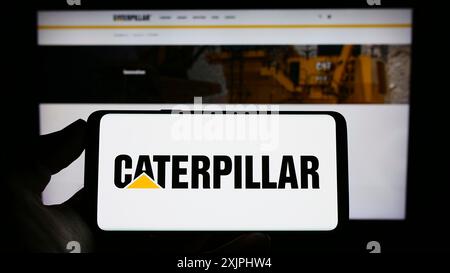 Stoccarda, Germania, 06-25-2023: Persona che detiene un telefono cellulare con il logo della società americana di attrezzature pesanti Caterpillar Inc. Sullo schermo davanti al Web Foto Stock