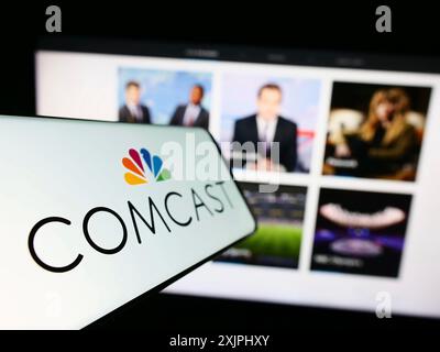 Stoccarda, Germania, 06-25-2023: Telefono cellulare con logo della società americana di telecomunicazioni Comcast Corporation sullo schermo davanti al sito web. Foto Stock