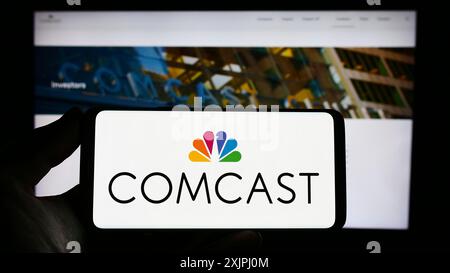 Stoccarda, Germania, 06-25-2023: Persona con smartphone con logo della società di telecomunicazioni statunitense Comcast Corporation sullo schermo di fronte Foto Stock