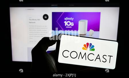 Stoccarda, Germania, 06-25-2023: Persona che detiene il cellulare con il logo della società di telecomunicazioni statunitense Comcast Corporation sullo schermo di fronte Foto Stock